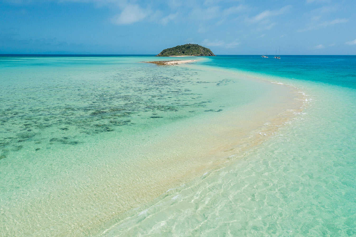 small mountain island on the horizon with sandbar snaking its way to the island with turquise waters eitherside