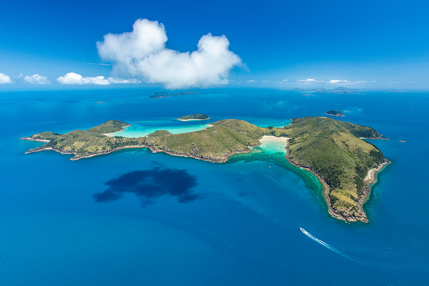 green mountainous island surrounded by green sandy beaches with clouds above casting a shadow over the water