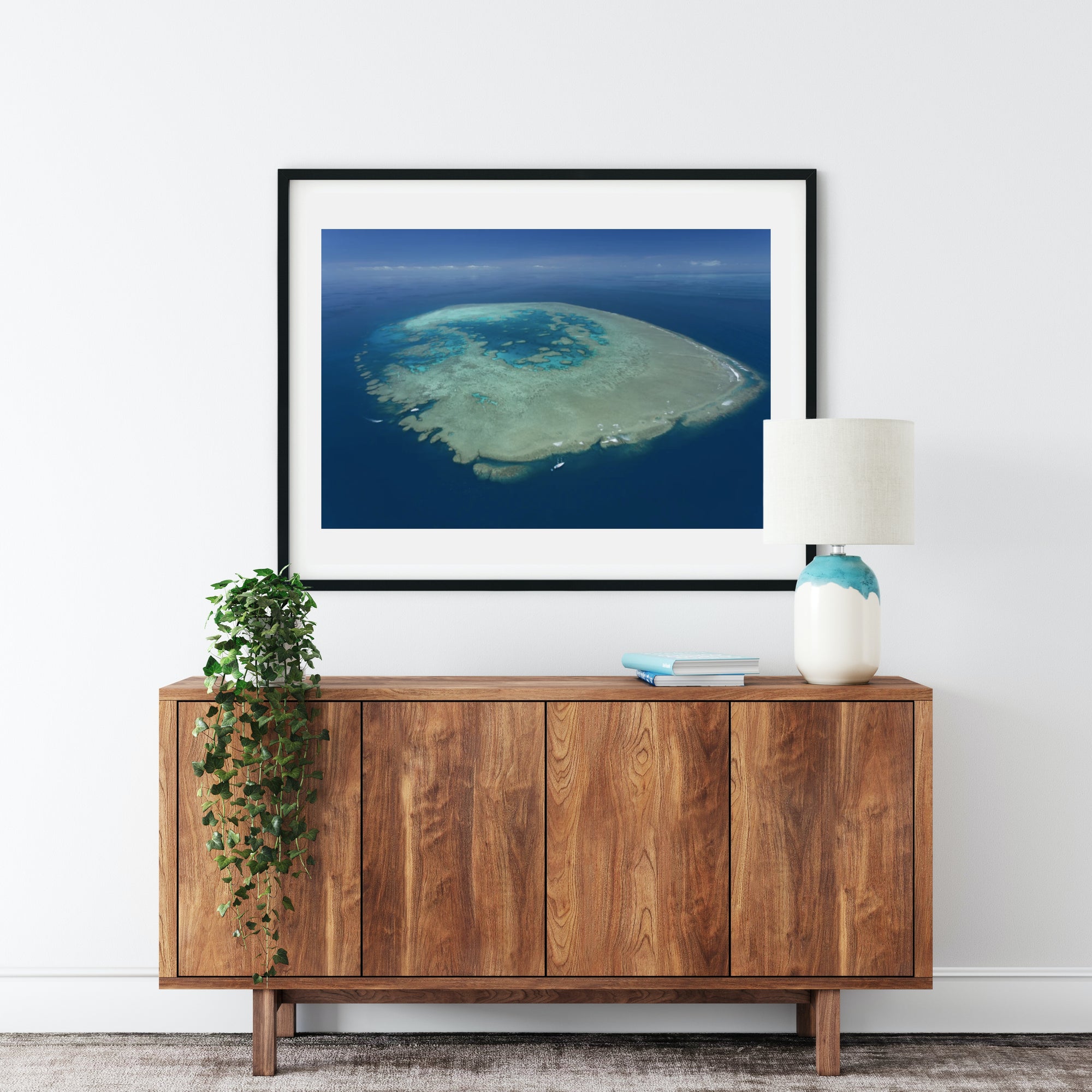 blue waters and sky surrounding large reef island waves breaking with sailing vessel in bottom left