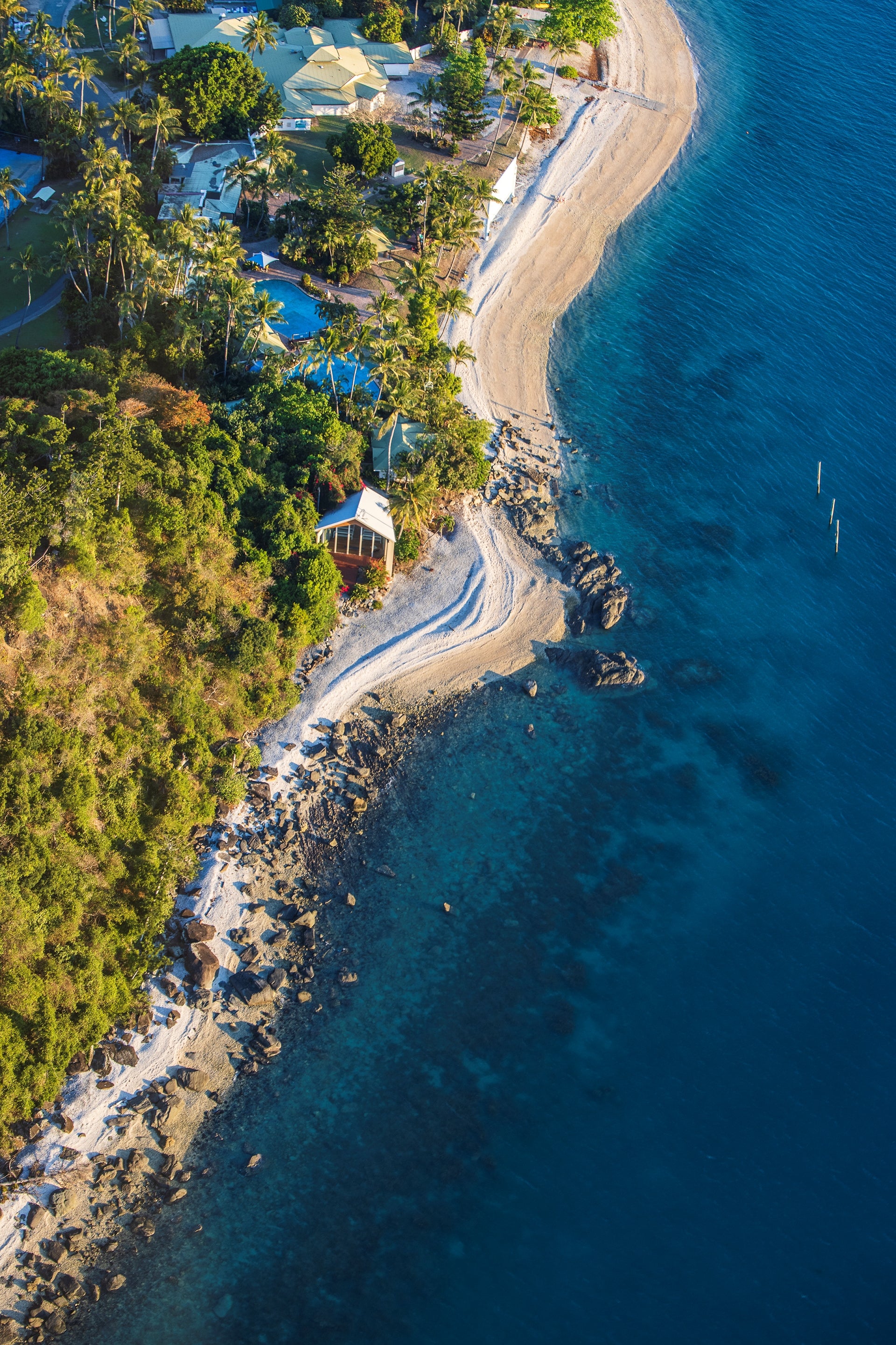 from above coastline with water on the right rocky sand beach, buildings and a chapel on the shoreline