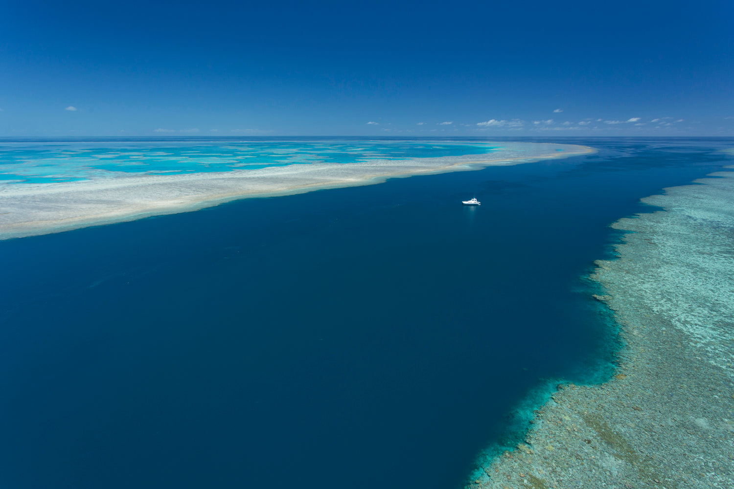 looking down on deep channel of water with large boat on anchor between fringing reef