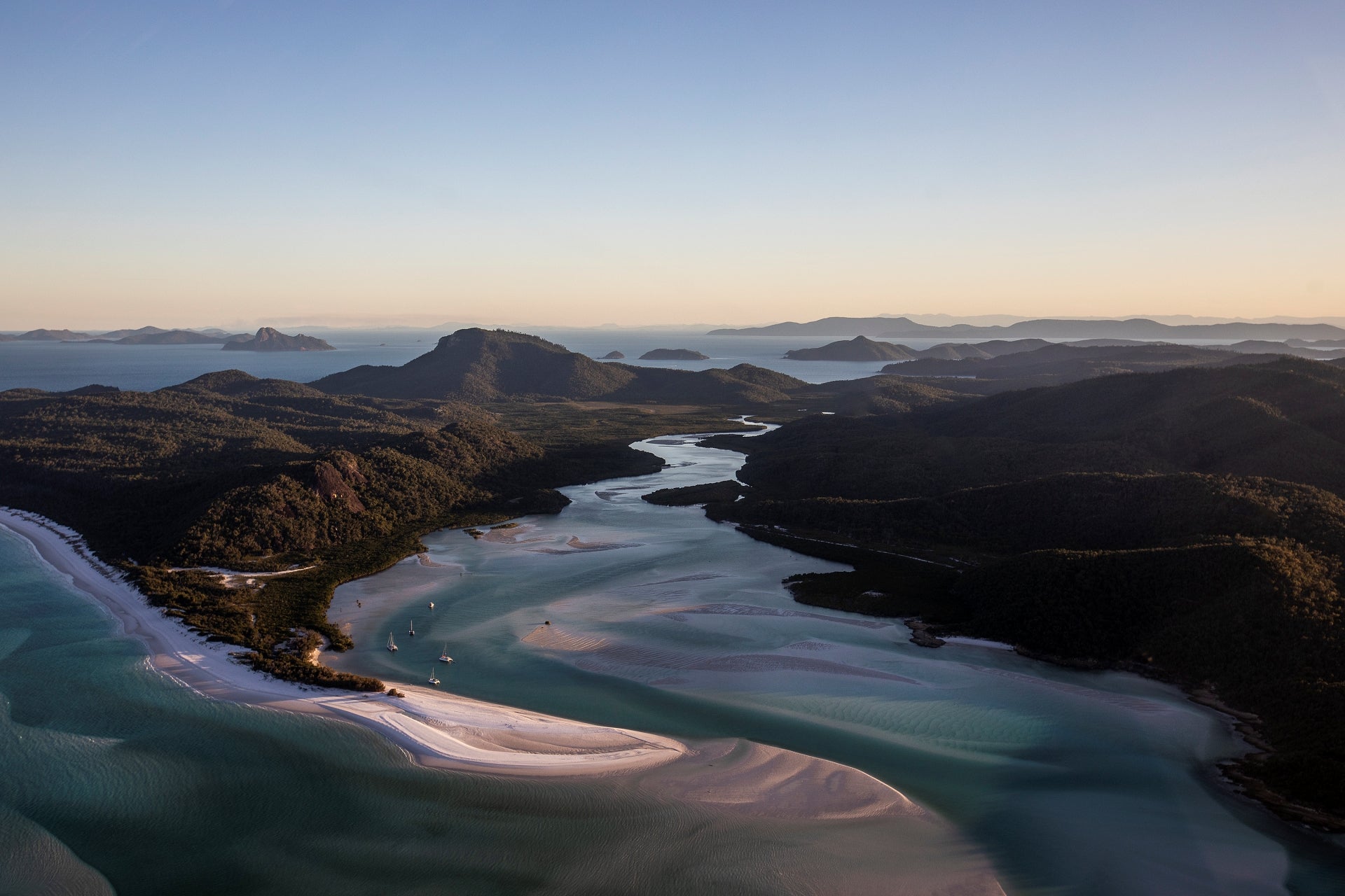 afternoon light casting across the mountain islands across several sailing vessels