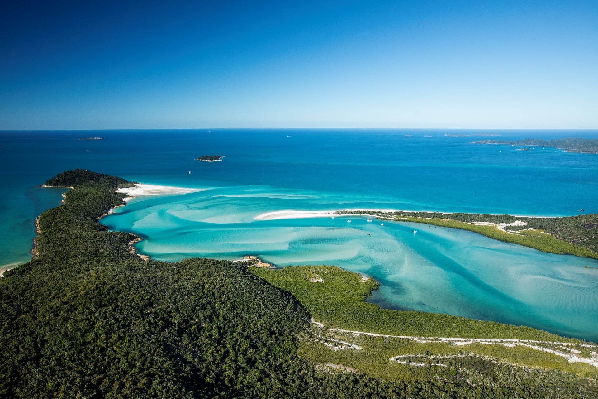 blue and turquiose water swirling amongst white sands of the tide changing sailing vessels on anchor