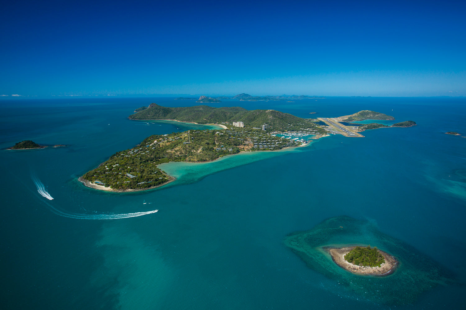 aerial of large holiday island with highrise, marina and airport boats motoring around the corner