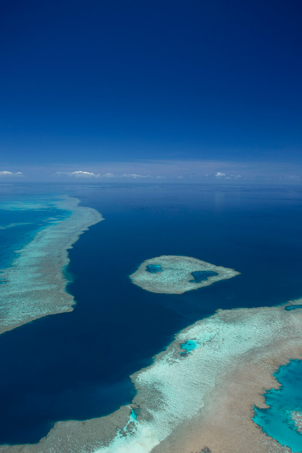 aerial of blue ocean and sky with fringing reef and an island of coral reef creating turquiose coloured water