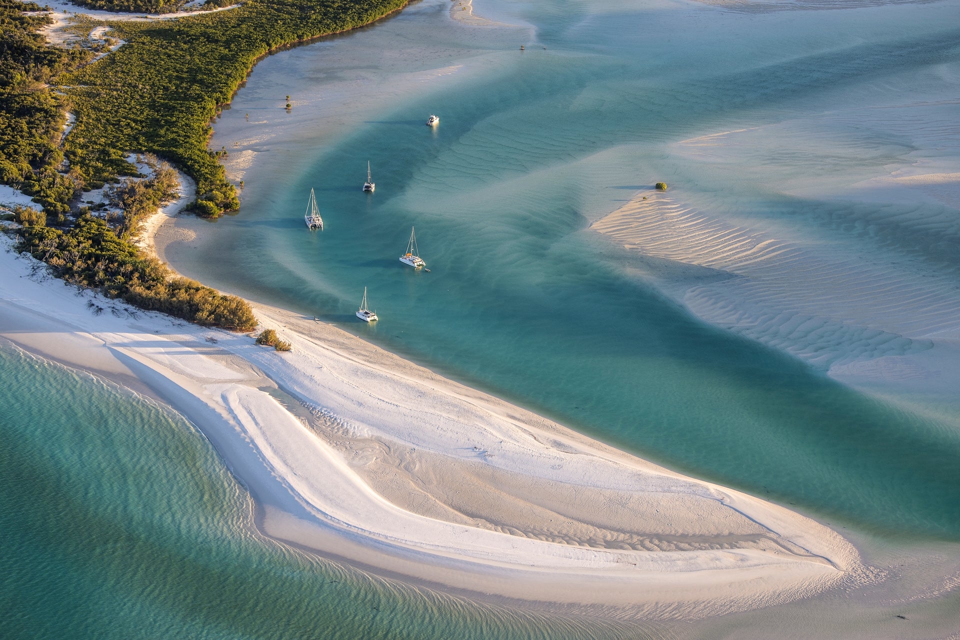 afternoon light casting shadow across the sailing vessels on anchor with turquiose waters surrounding a white sand bar