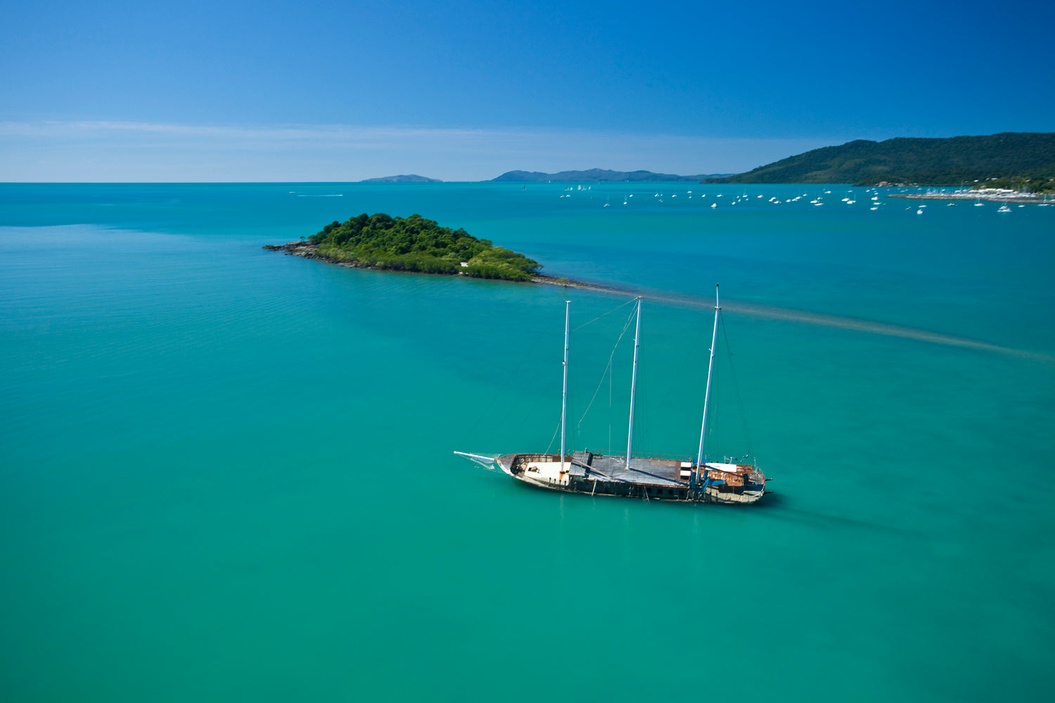 island with mainland and sailing vessels in the background with grounded damaged sailing vessel