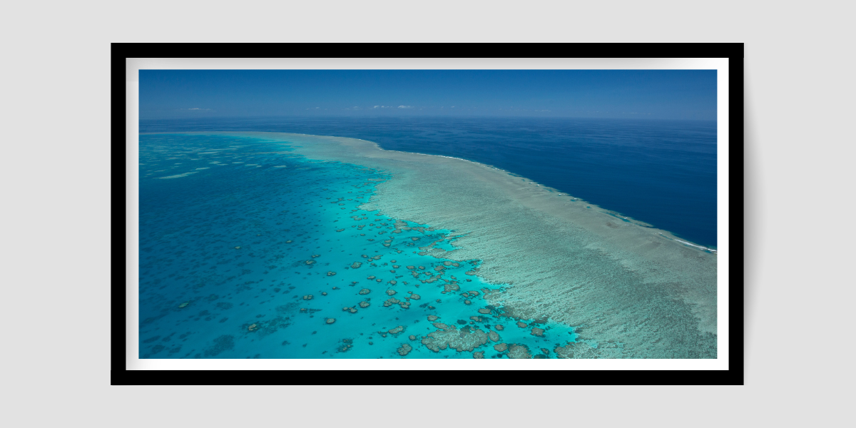 large island of coral reef with waves breaking on the surface and the darker deep blue is beyond