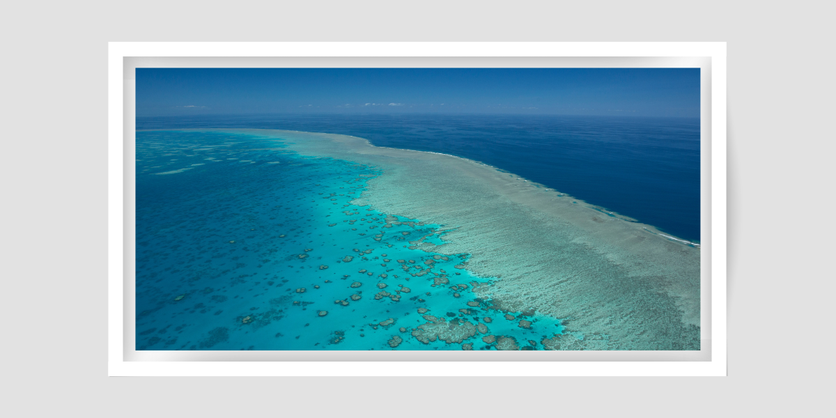 large island of coral reef with waves breaking on the surface and the darker deep blue is beyond