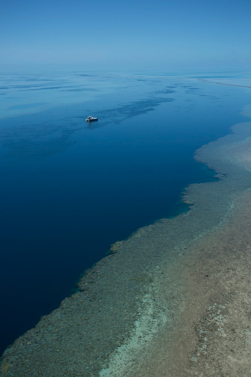 open blue ocean with a brown reef in the foreground a vessel on anchor amongst calm blue waters beyond