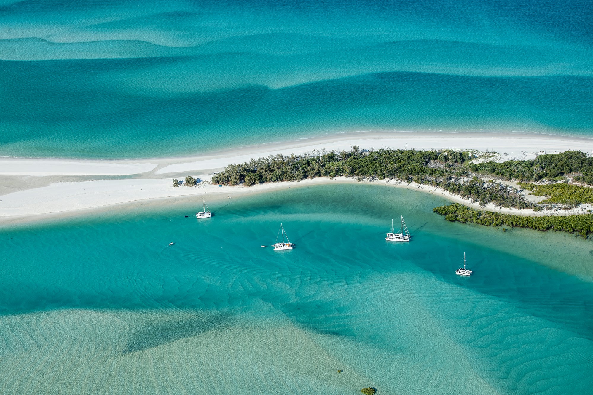 4 vessels anchored within a protected calm bay and different coloured ocean waters beyond