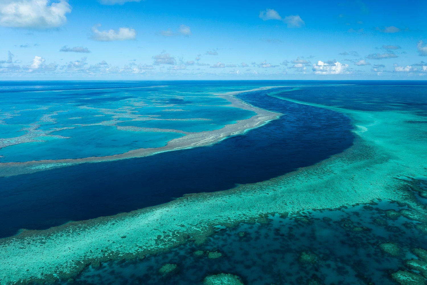 4 vessels anchored within a protected calm bay and different coloured ocean waters beyond