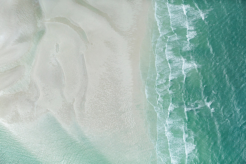 from right the turquiose water waves lap at the white sand on left
