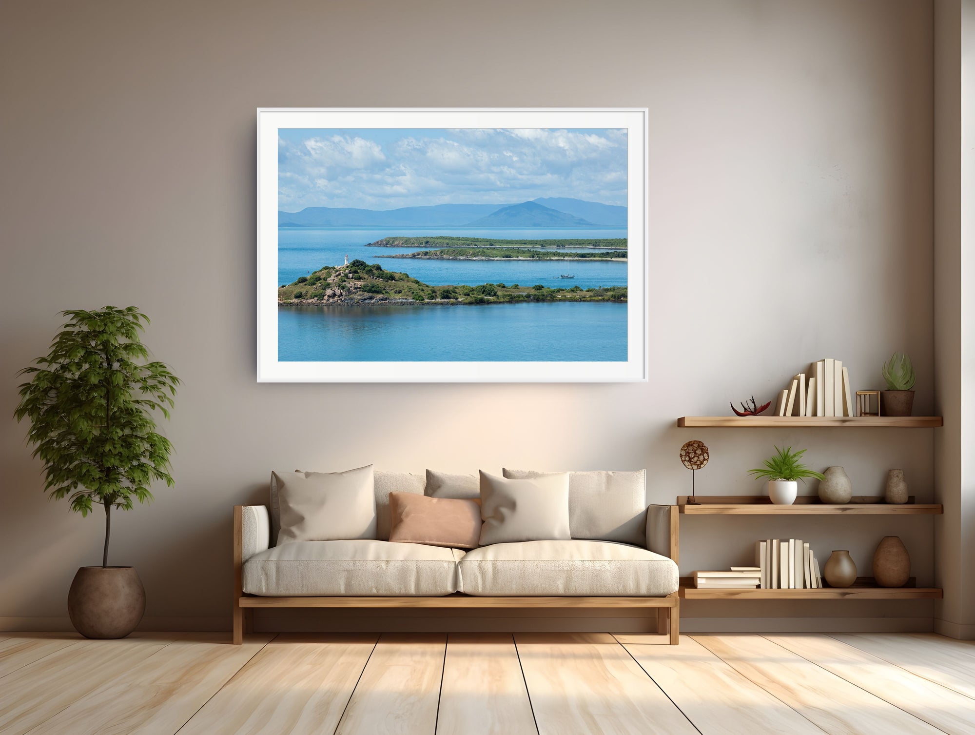 A framed landscape art print of a blue sea and green islands hangs on a beige wall above a light wood sofa in a modern living room setting.