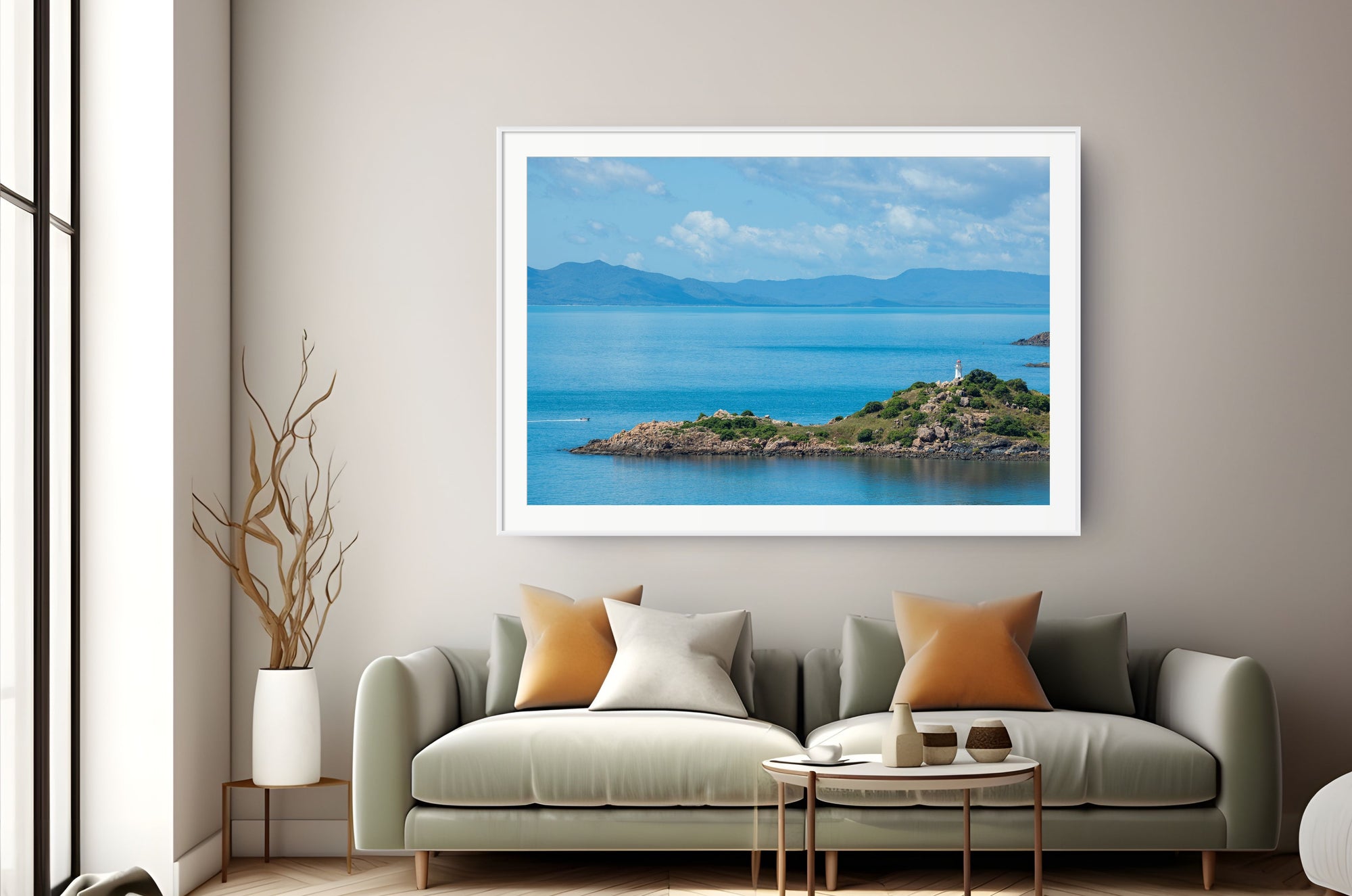 A framed landscape art print of a blue sea and island under a cloudy sky, displayed on a beige wall above a modern green sofa with decorative pillows.