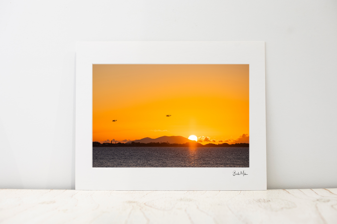 A Small photo mount featuring a vibrant orange and yellow sunset over water, displayed on a light marble surface against a neutral white wall.