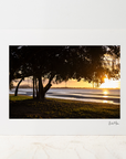 A large photo mount featuring a sunset over a shoreline with silhouetted trees, displayed against a white wall on a light marble surface.