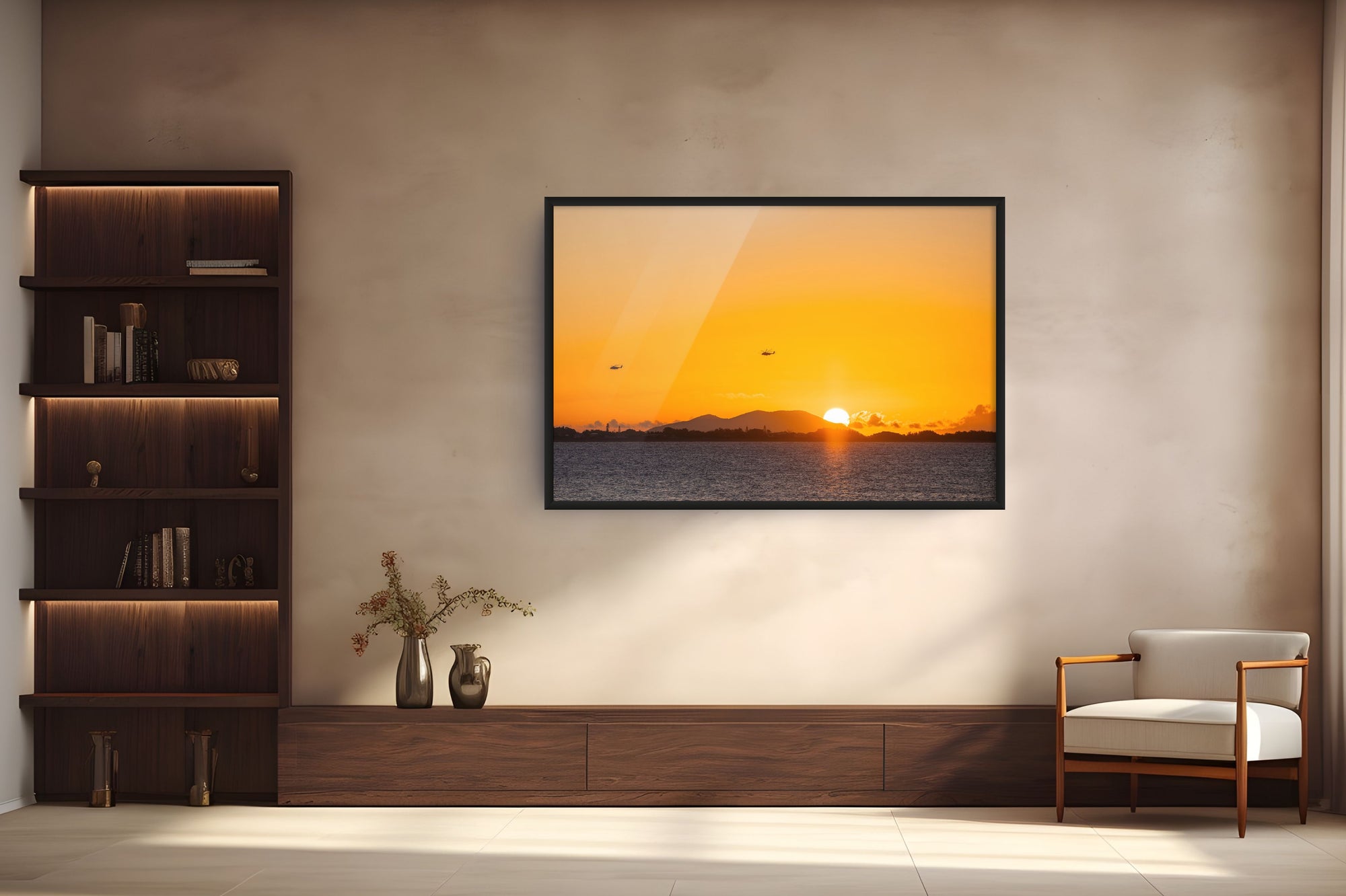A framed wall art print depicting a vibrant orange sunset over water, displayed on a textured beige wall in a modern living room setting with a wooden bookshelf and a white armchair.