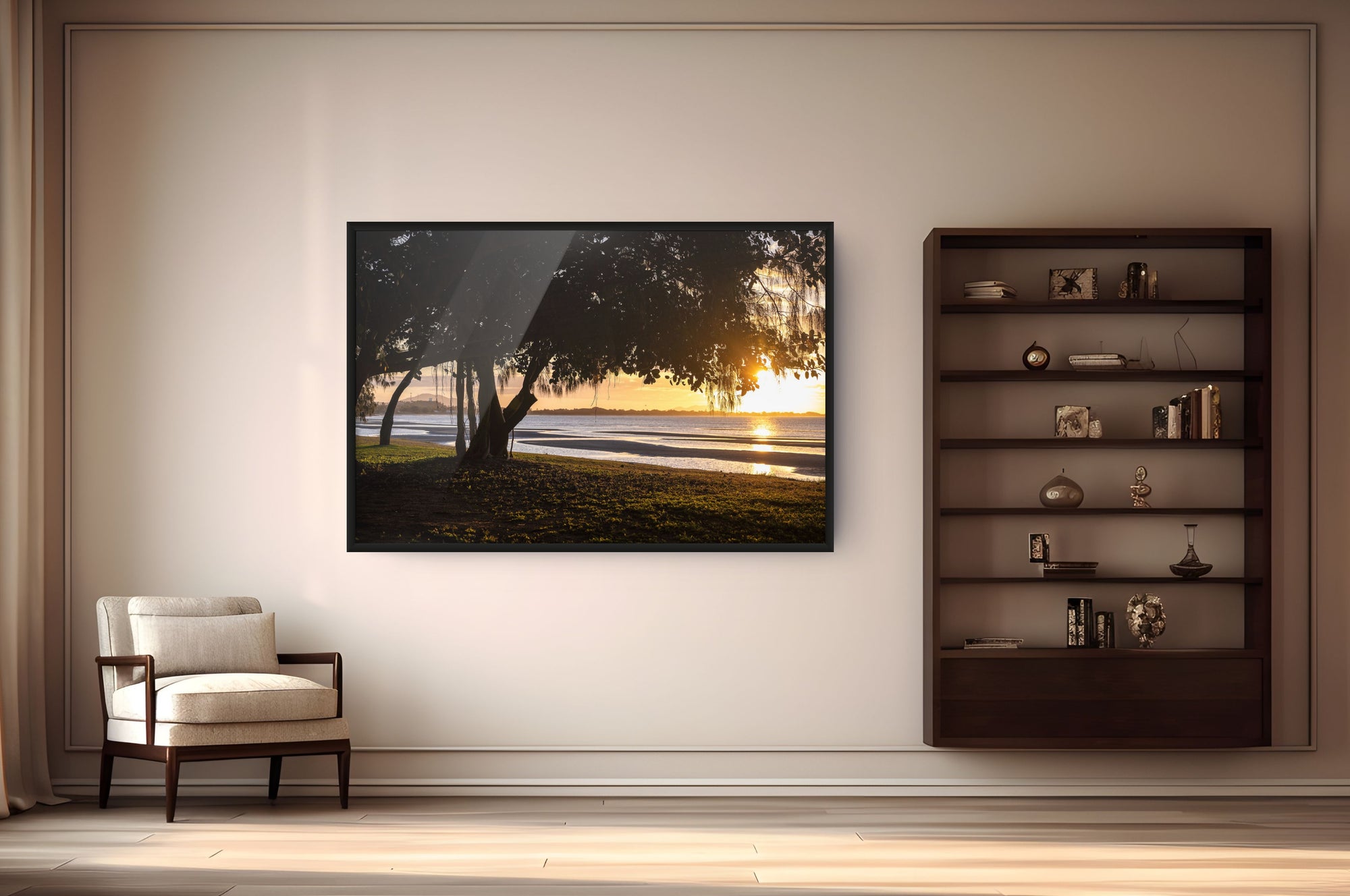 A framed wall art print depicting a sunset landscape with trees and water, displayed in a modern living room setting next to a dark wood bookshelf and an armchair.
