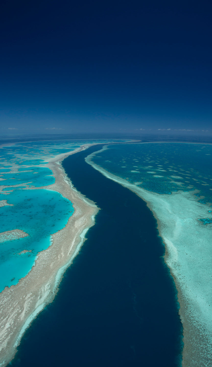 dark blue deep channel of water creating a river between green blue and brown fringing reef