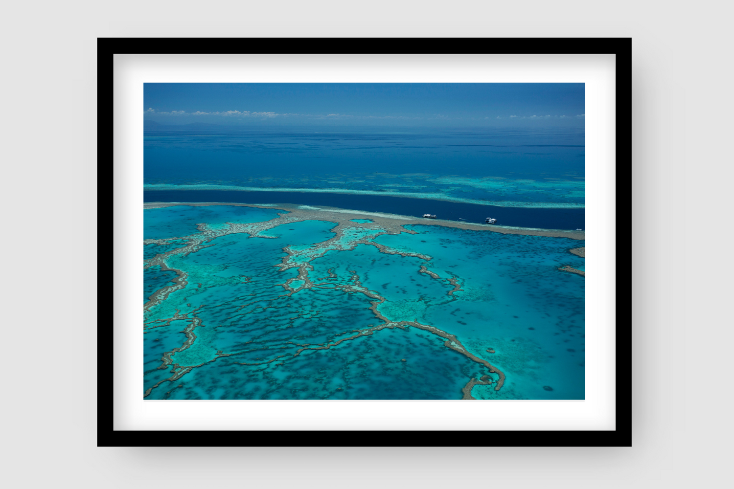 aerial of veiny coral reef amongst turquiose water deep water beyond with large boats on anchor