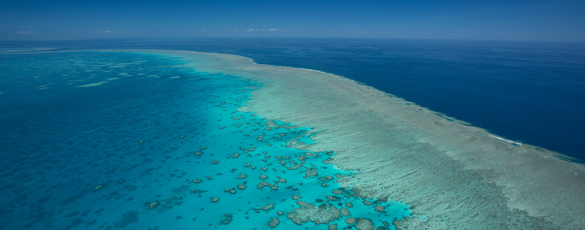 large island of coral reef with waves breaking on the surface and the darker deep blue is beyond