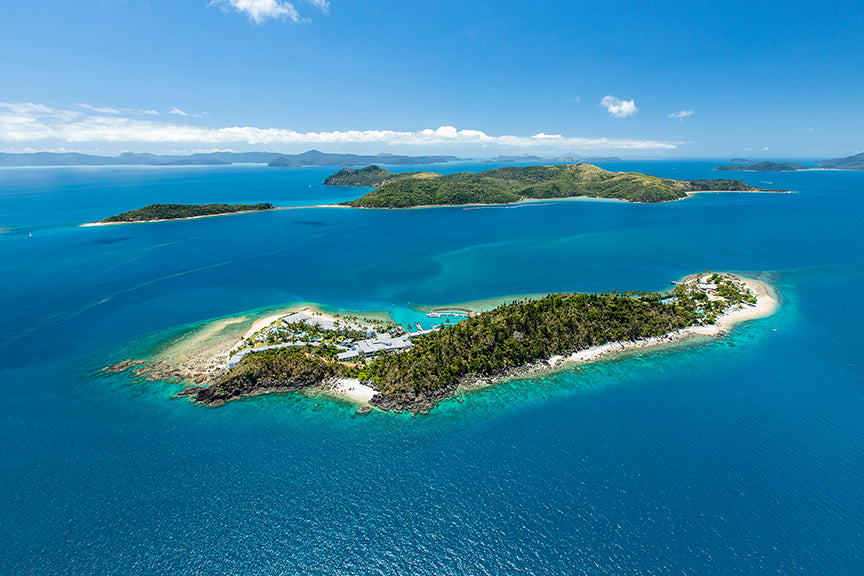 aerial of holiday island with marina and buildings surrounded by fringing reef
