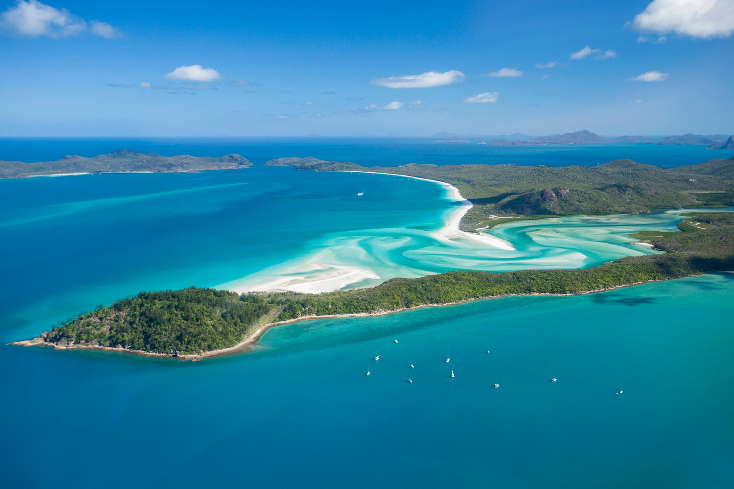 aerial of anchored sailing vessels at a bay with white sand swirling past the bay