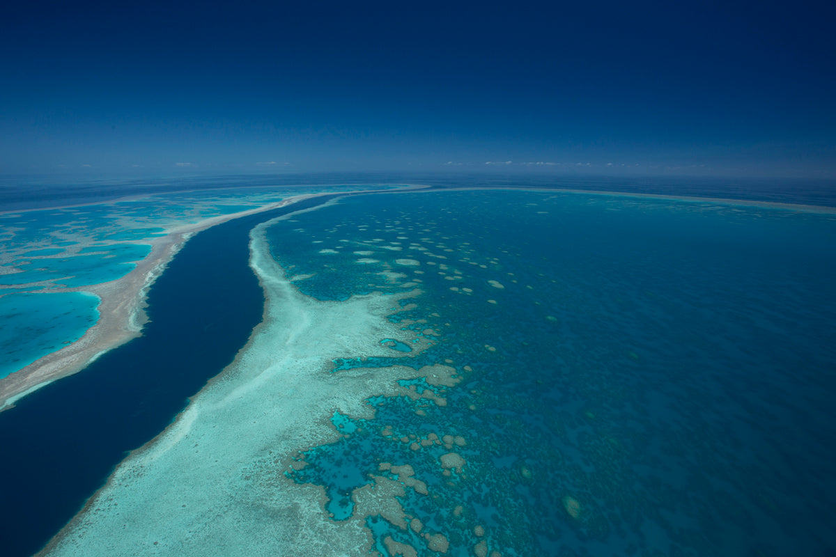 deep channel of dark ocean water flowing between 2 large island walls of blue green coral reef