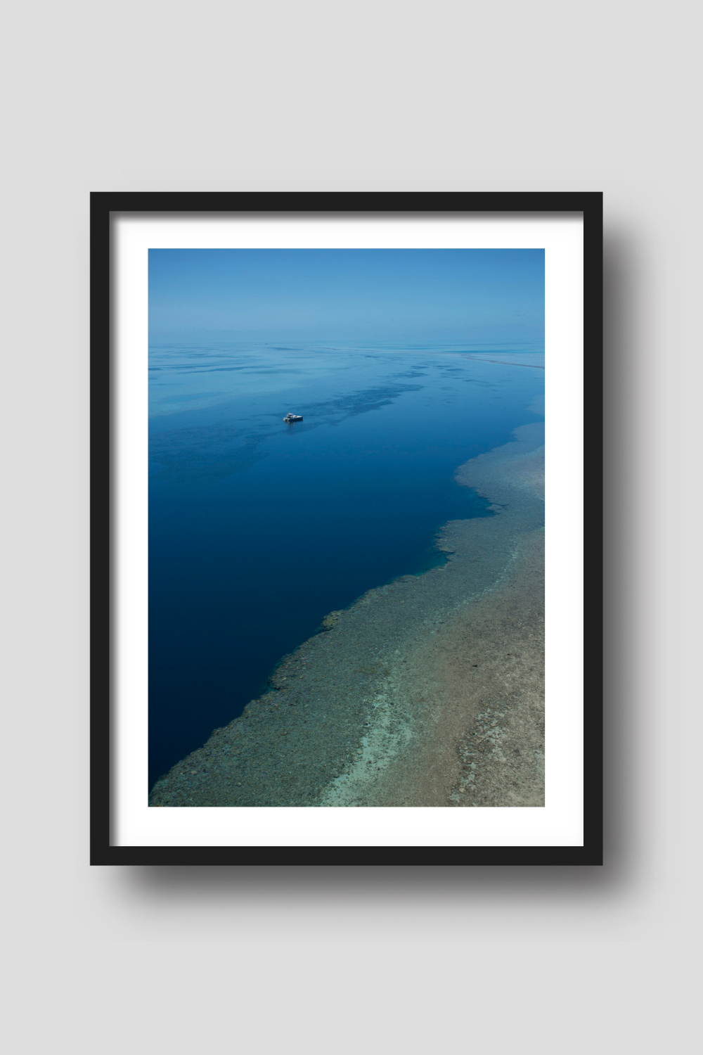 open blue ocean with a brown reef in the foreground a vessel on anchor amongst calm blue waters beyond