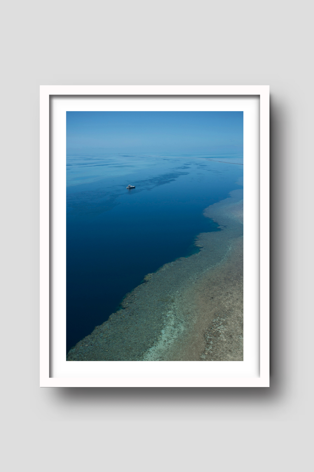 open blue ocean with a brown reef in the foreground a vessel on anchor amongst calm blue waters beyond